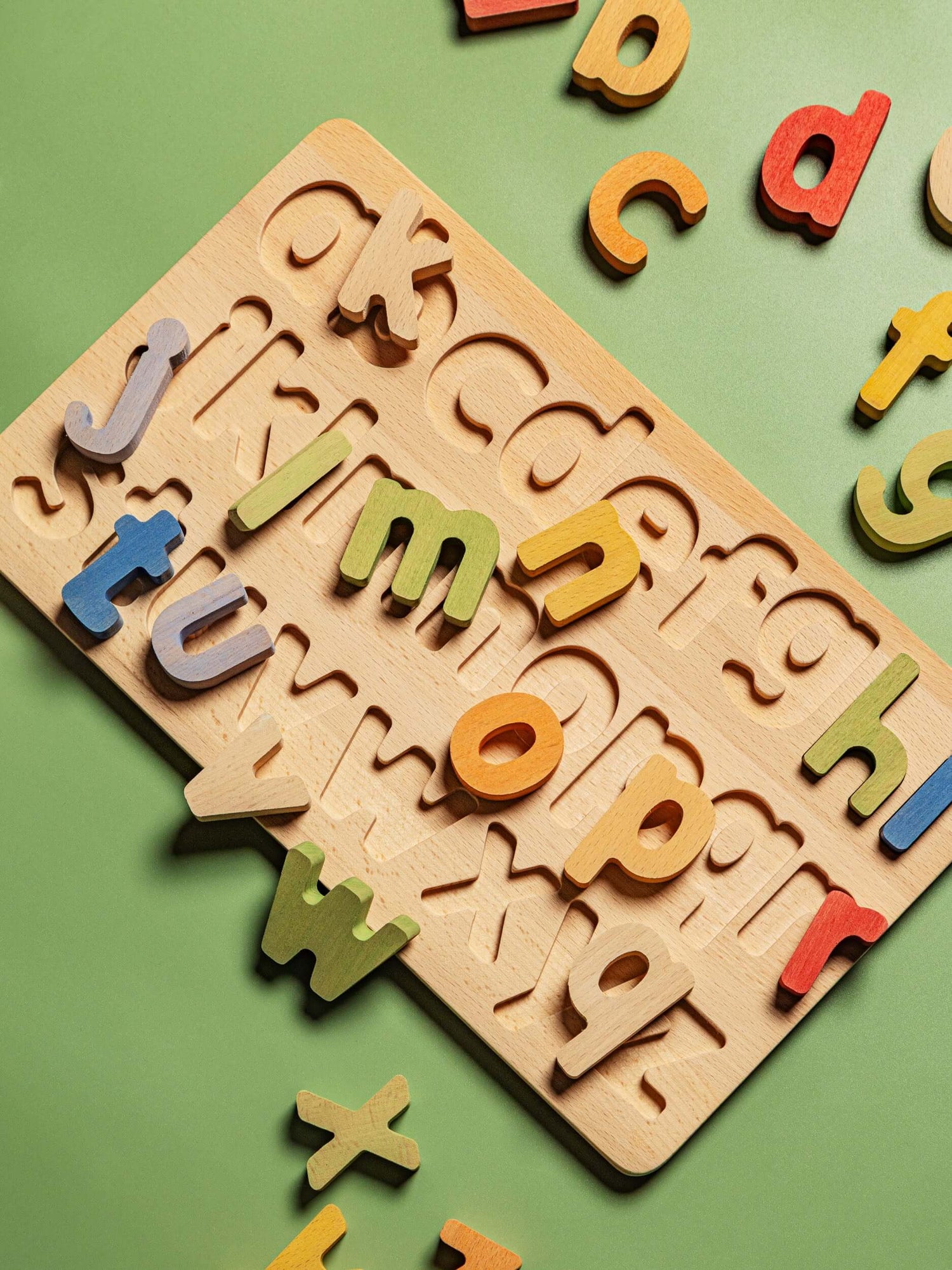 Colorful wooden letters from the educational puzzle set displayed on a green background.