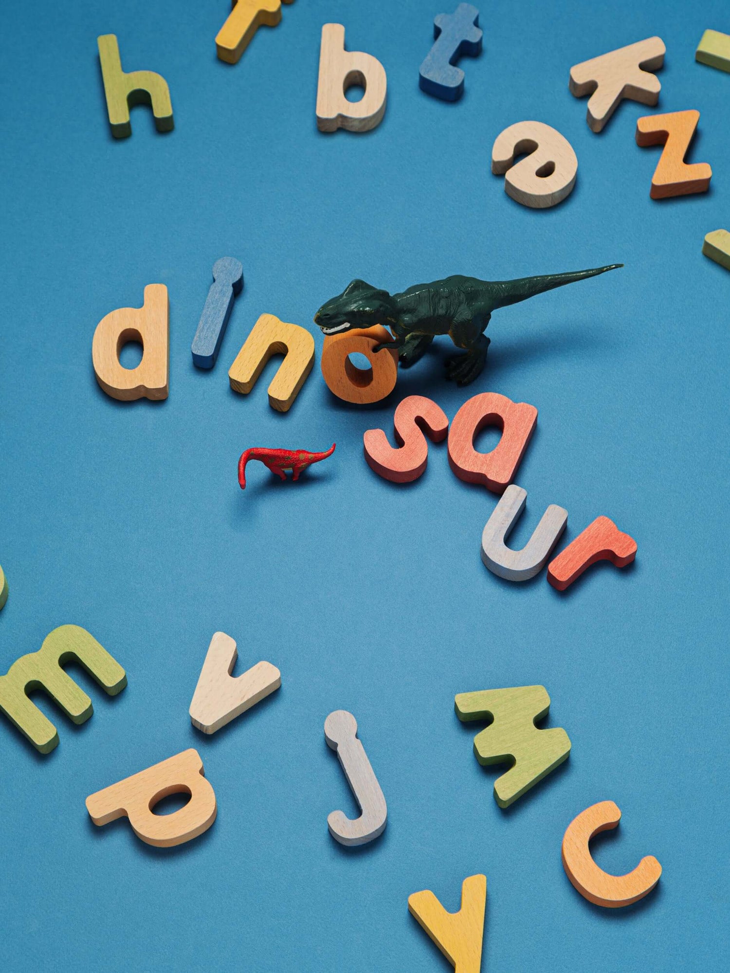Colorful letters scattered with dinosaur toys on blue background, showcasing an educational puzzle set.