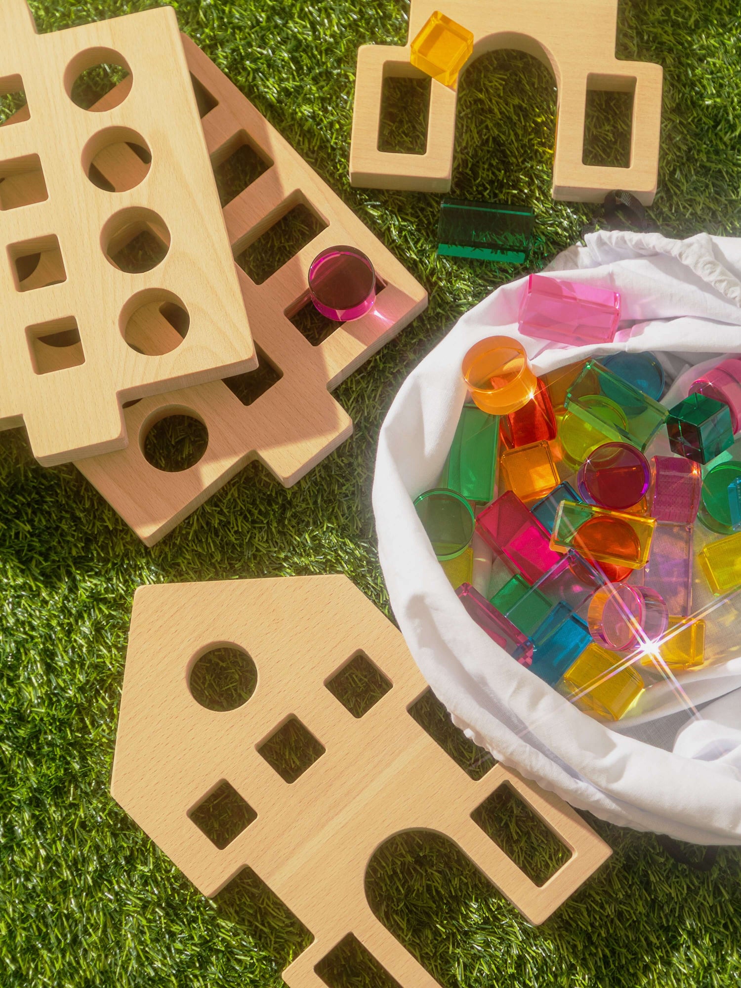 Rêve House Set modular wooden building set pieces arranged on grass with colorful translucent shapes in a bag.