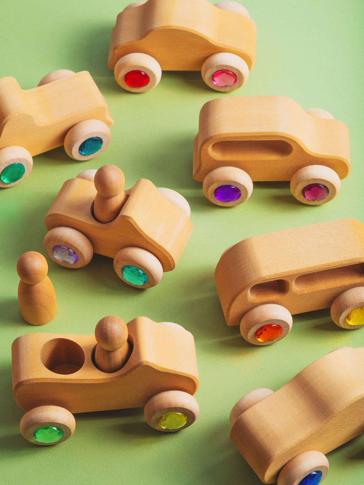 Otto wooden toy vehicles with gemstone wheels displayed on a green background, showcasing colorful wheels and natural wood design.