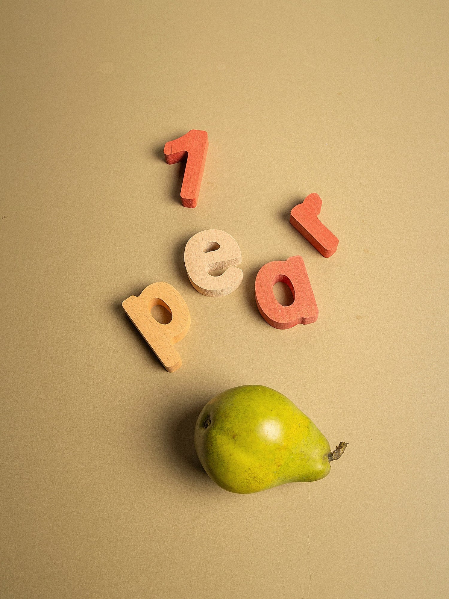 Colorful wooden letters spelling '1 pear' with a green pear on a beige background.