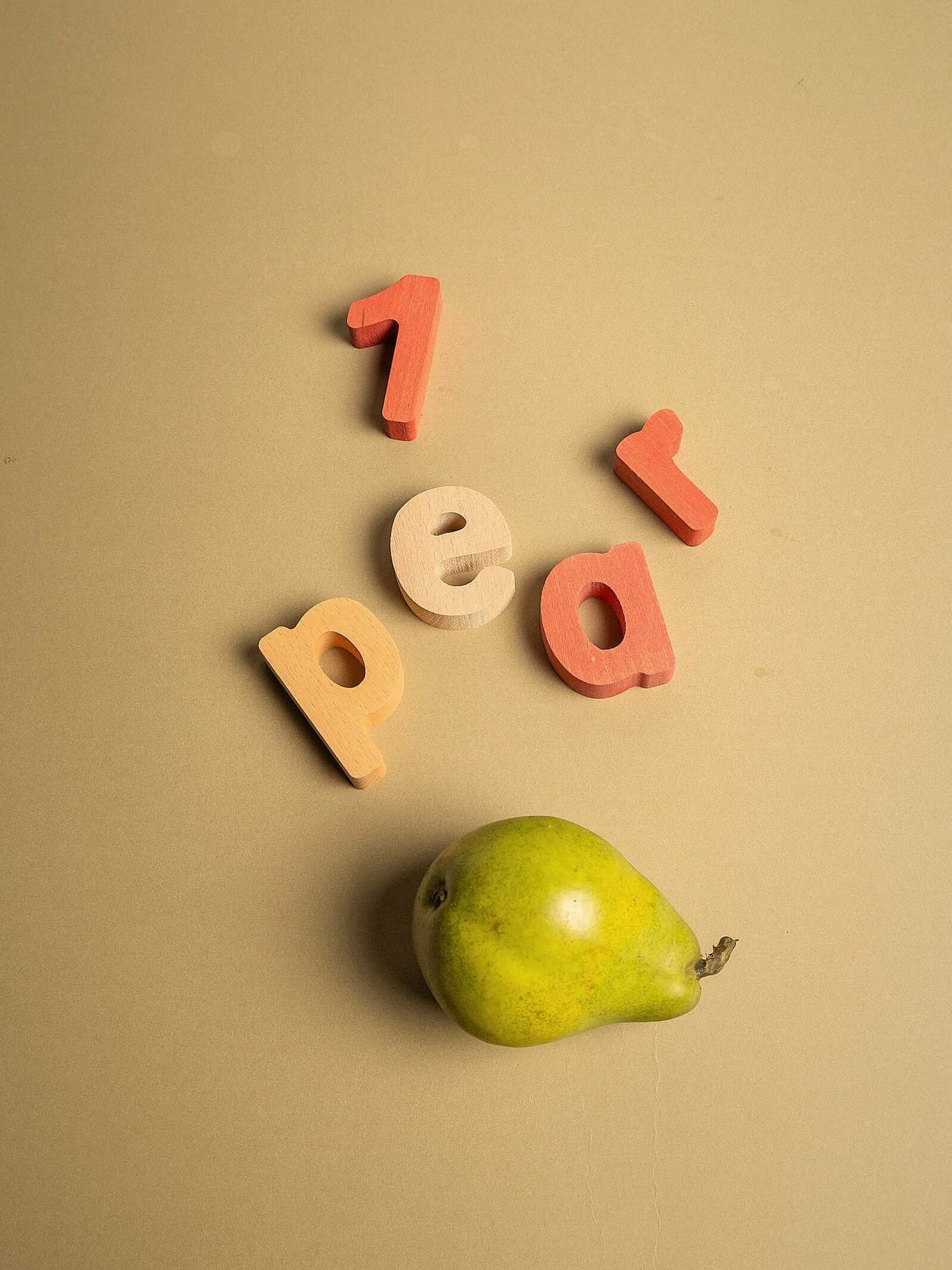 Colorful wooden letters spelling '1 pear' with a green pear on a beige background.
