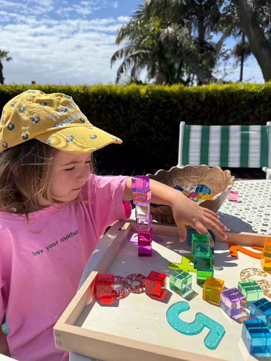 Child playing with colorful transparent blocks outdoors on a sunny day.