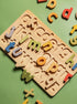 A wooden alphabet puzzle board with colorful alphabet letter pieces scattered on a solid green background.