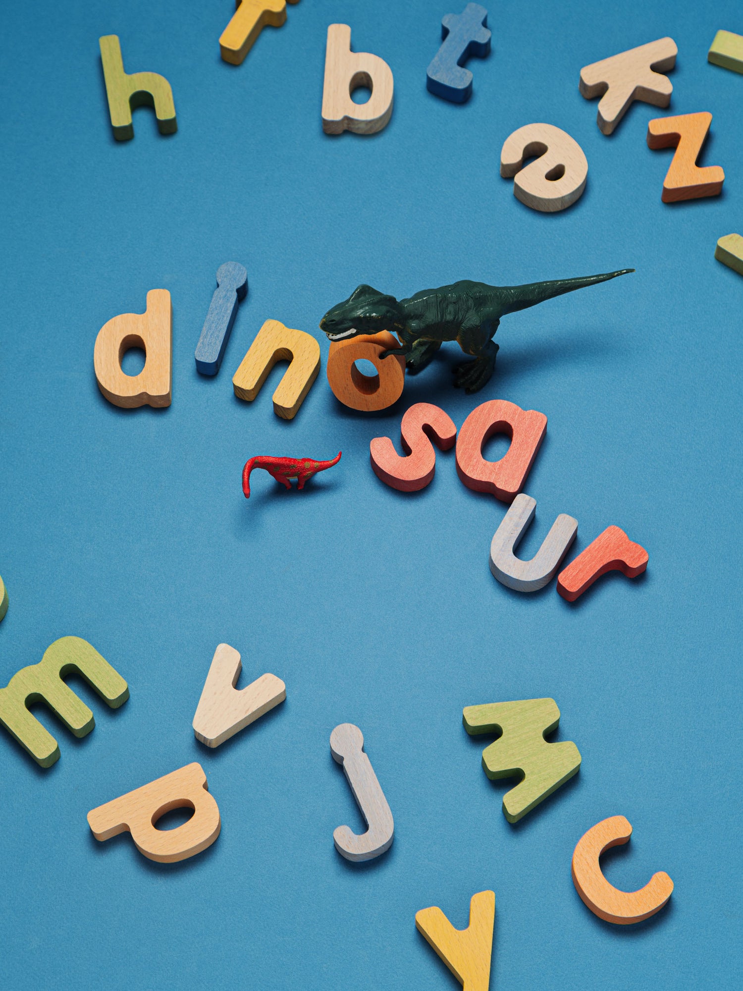 Colorful letters scattered with dinosaur toys on blue background, showcasing an educational puzzle set.
