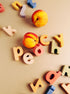 Two real peaches arranged among scattered colorful wooden letters spelling out 'peach' on a warm beige background.