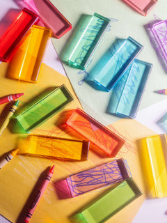 Colorful Illume Tower acrylic stacking blocks scattered among crayons on vibrant paper.
