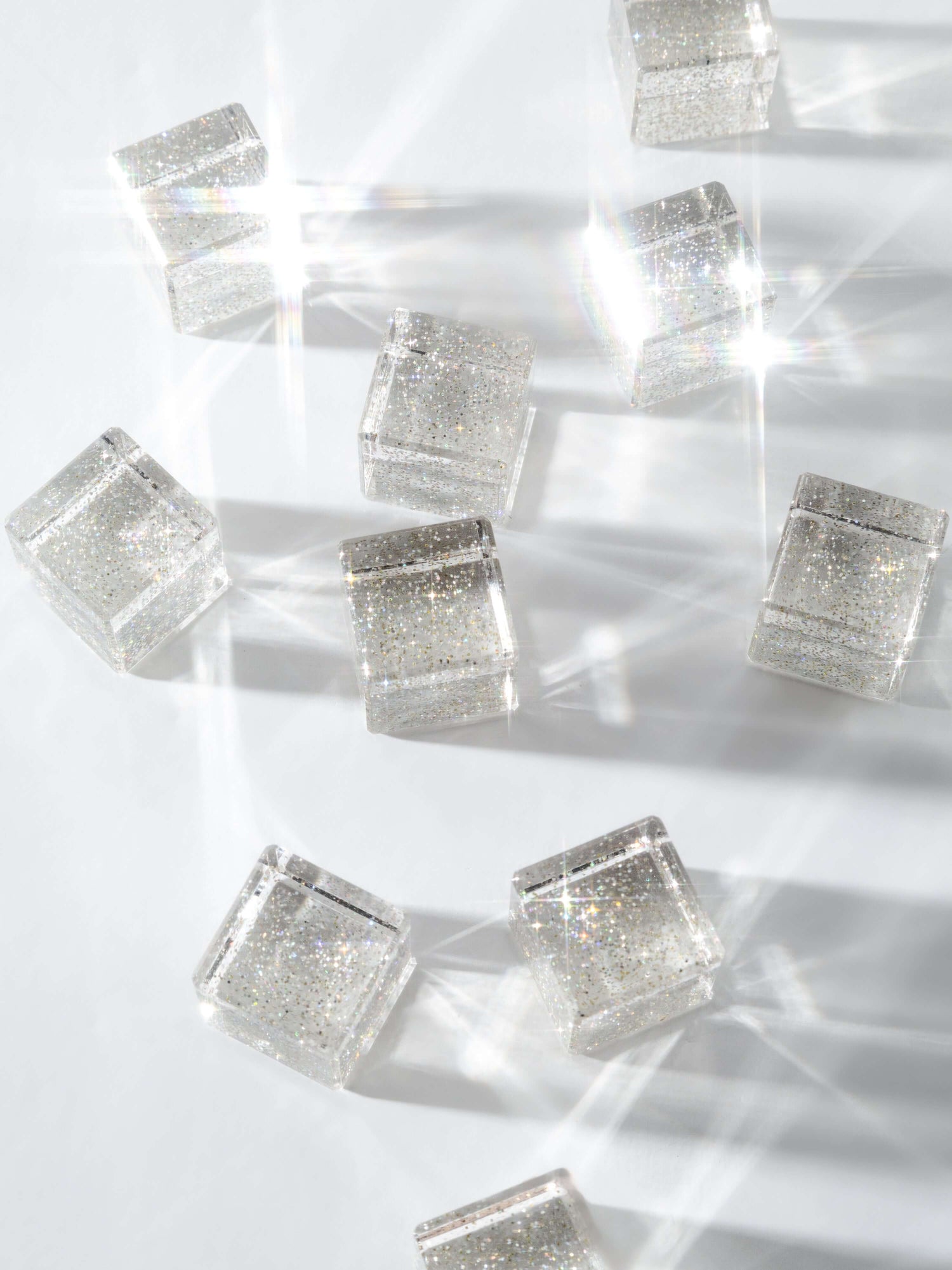 Cosmic cube acrylic glitter blocks scattered on a surface, reflecting light and creating sparkles.