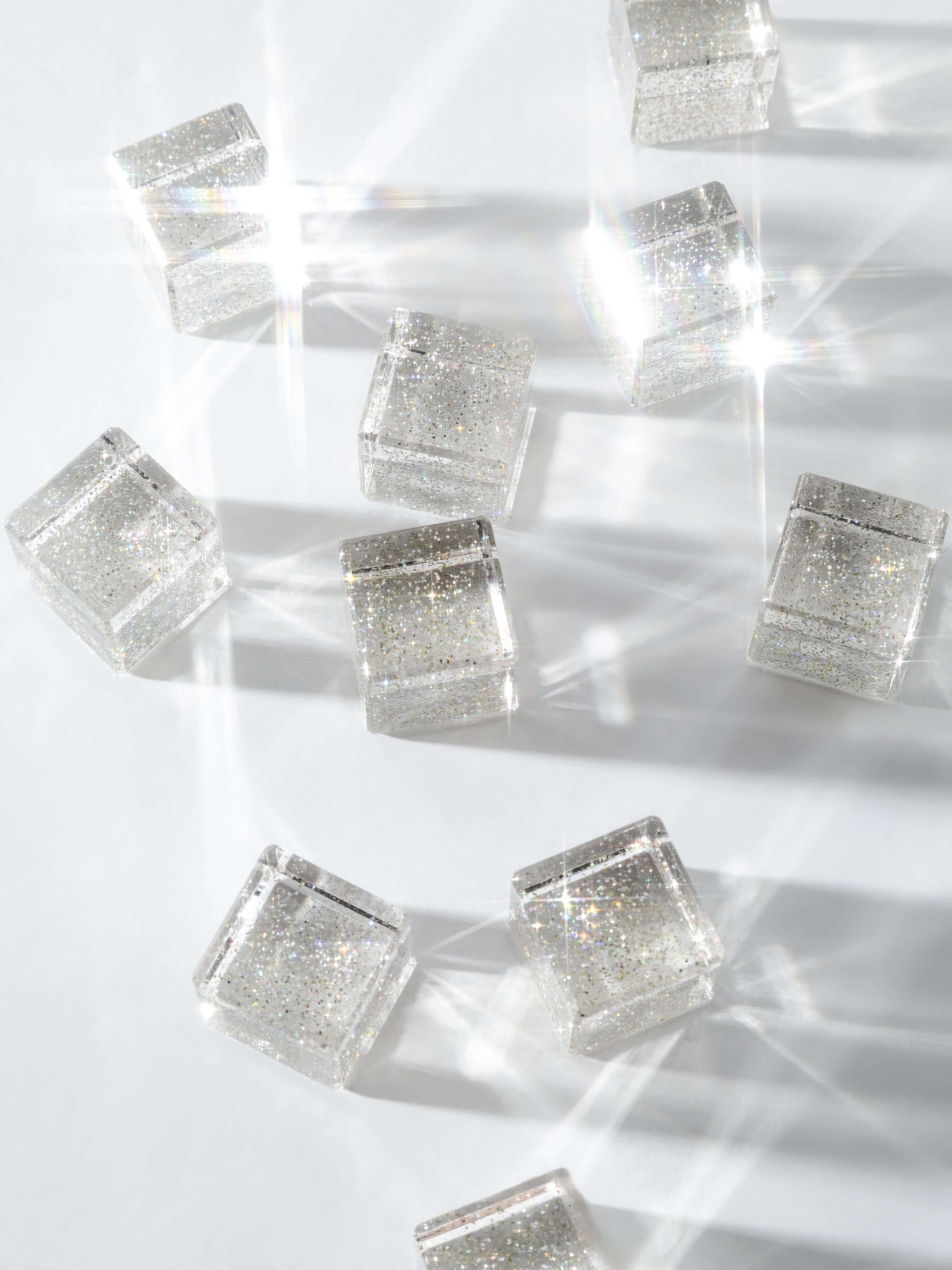 Cosmic cube acrylic glitter blocks scattered on a surface, reflecting light and creating sparkles.