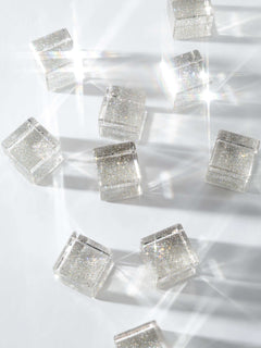 Cosmic cube acrylic glitter blocks scattered on a surface, reflecting light and creating sparkles.