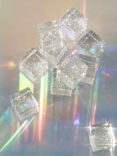 Cosmic cube acrylic glitter blocks scattered on a reflective surface, showcasing their sparkle and translucent beauty.