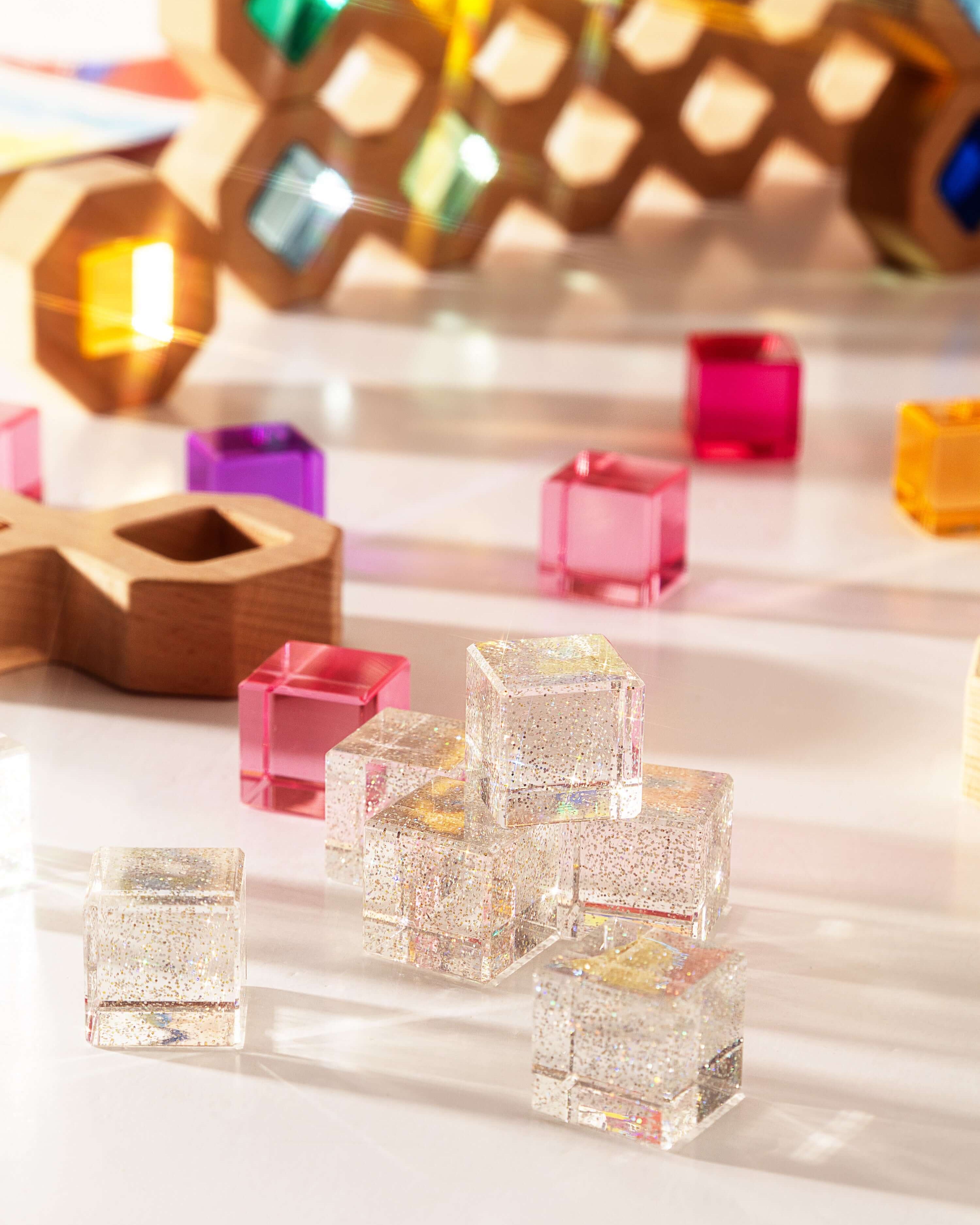 Colorful cosmic cube acrylic glitter blocks arranged on a bright surface, reflecting light and textures.