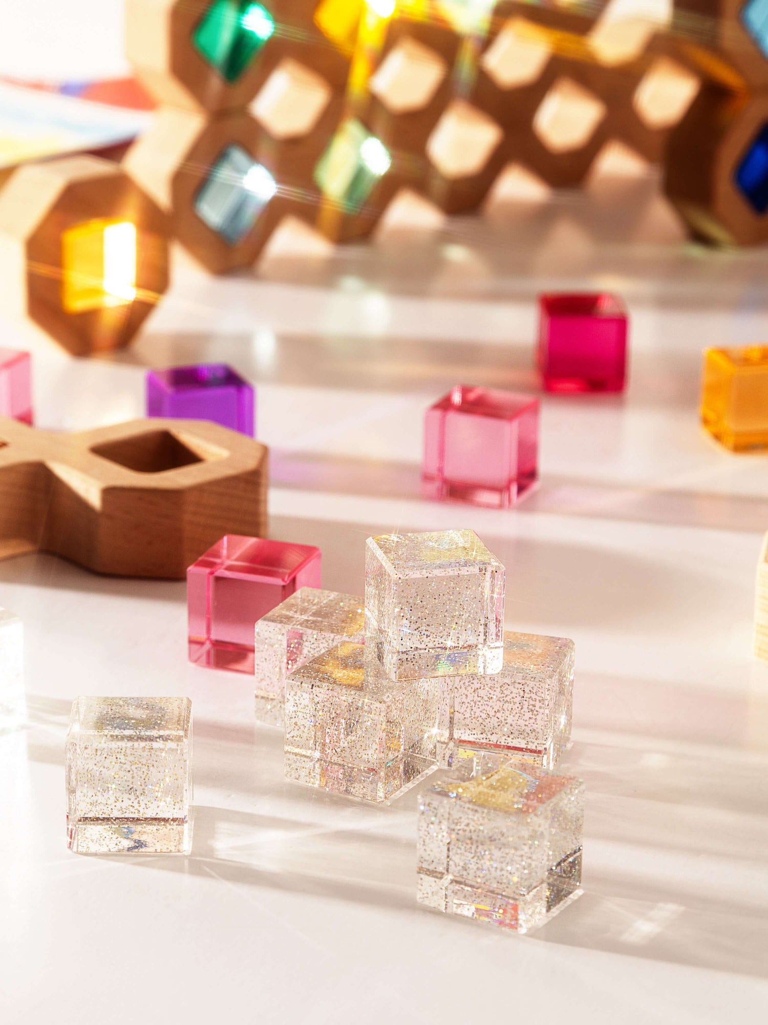 Colorful cosmic cube acrylic glitter blocks arranged on a bright surface, reflecting light and textures.