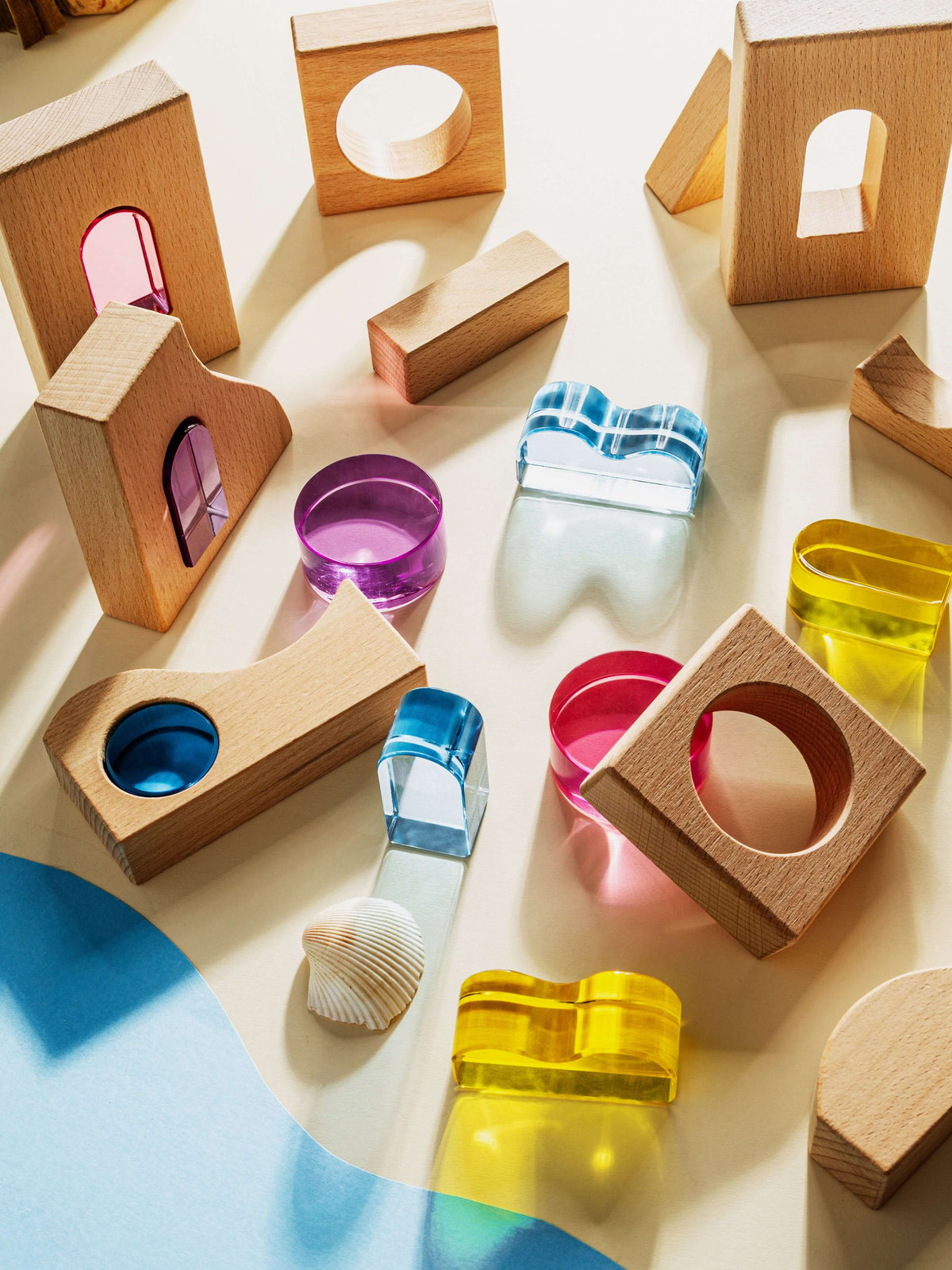 Colorful acrylic and beechwood pieces from the Laguna Block Set arranged on a sandy surface, inspired by coastal themes.