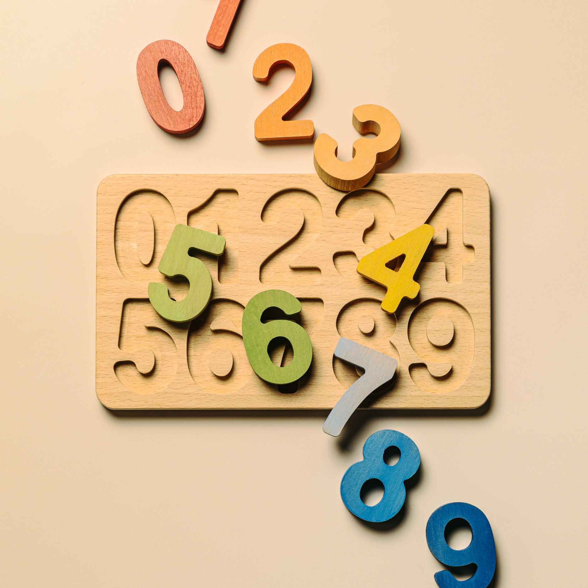 A wooden number puzzle board with carved slots and colorful loose number pieces on a warm beige background.