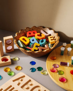 Colorful educational puzzle set with letters in a bowl, accompanied by gems and tools for hands-on learning.