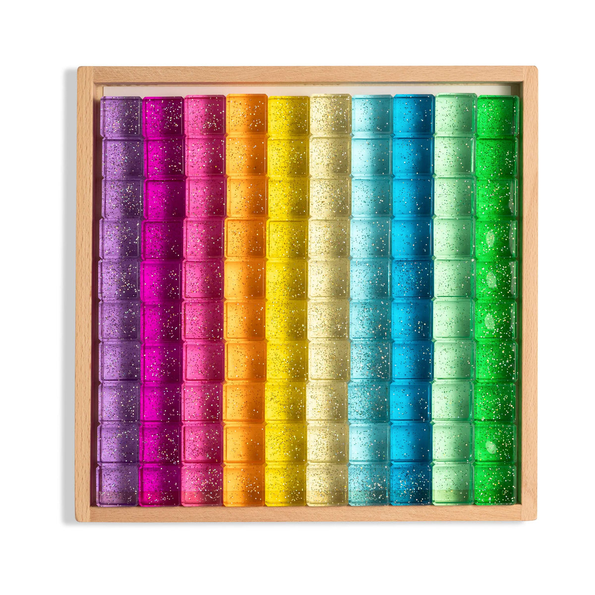 Lumi glitter acrylic building blocks arranged in a rainbow pattern in a wooden tray, showcasing their translucent shimmer.