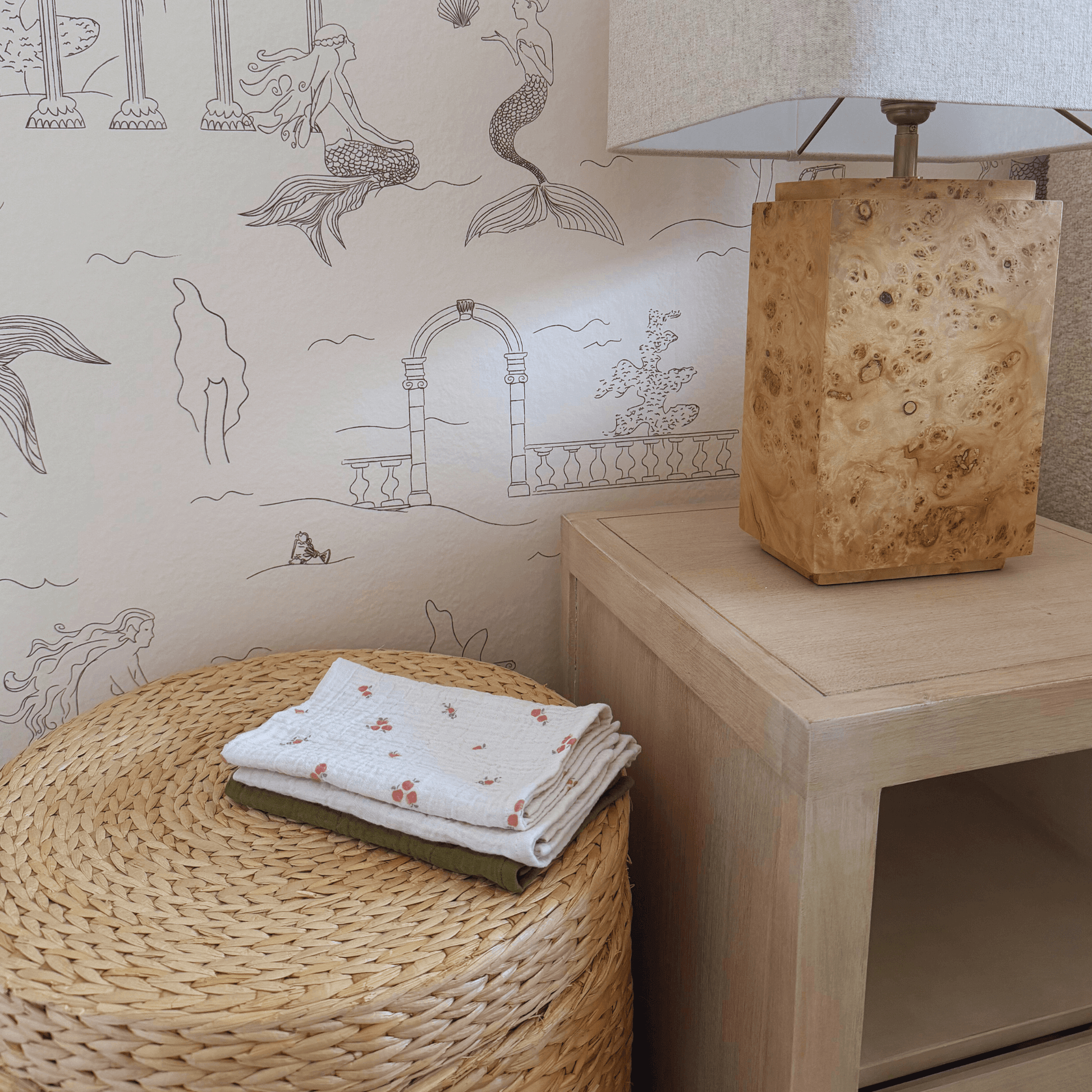 Pomme Burp Cloths neatly folded on a woven basket next to a wooden lamp in a stylish nursery setting.