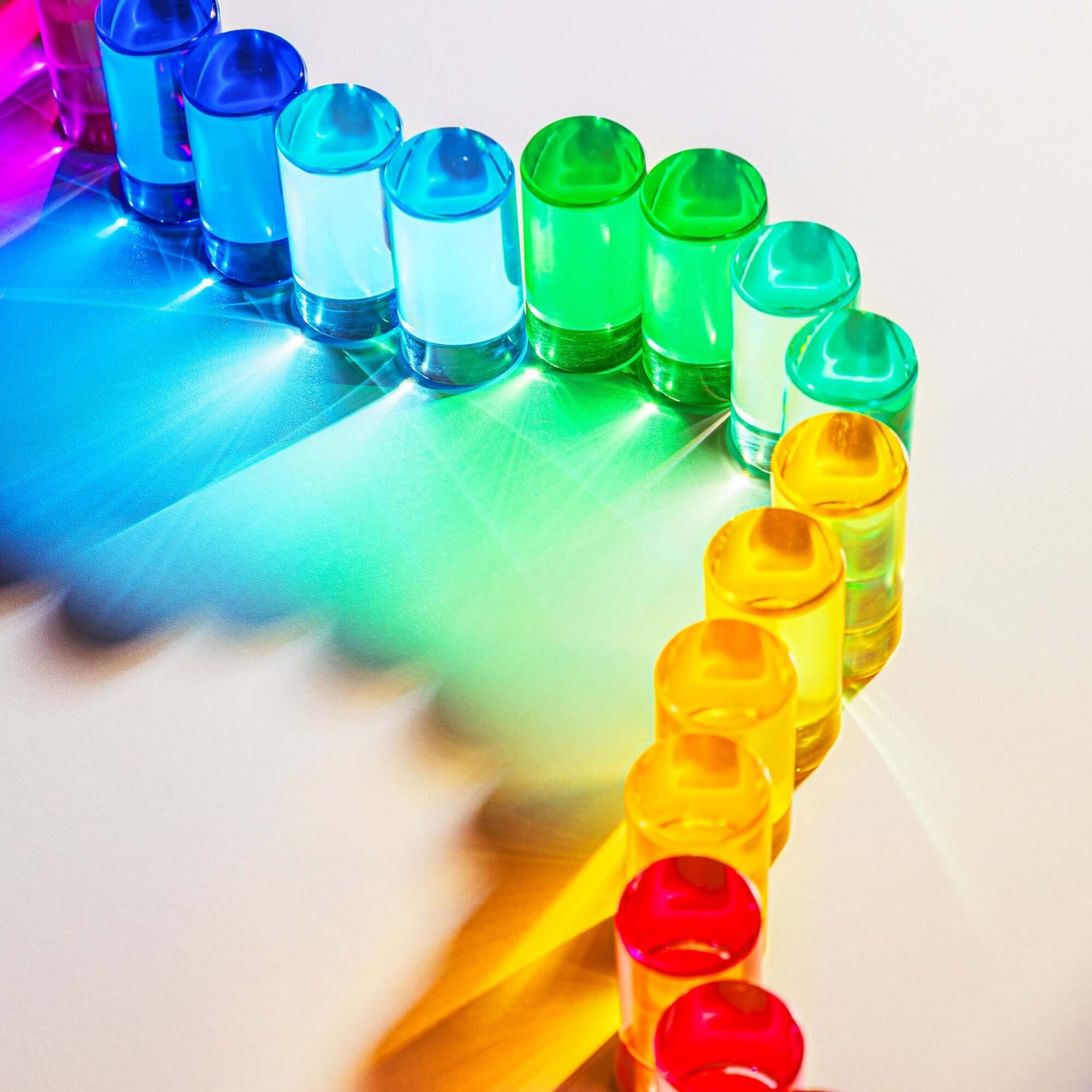 Colorful lucite blocks arranged in a rainbow pattern on a white surface.