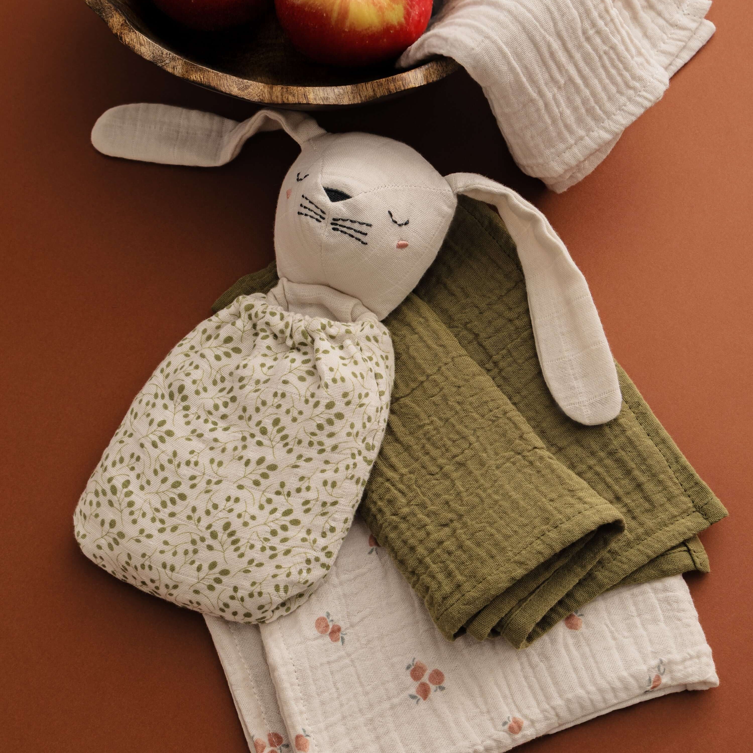 Pomme Burp Cloths with a cute rabbit toy and fresh apples in a rustic setting, showcasing organic cotton baby essentials.