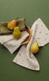 Pomme Burp Cloths displayed with organic muslin and decorative pears on a green background.