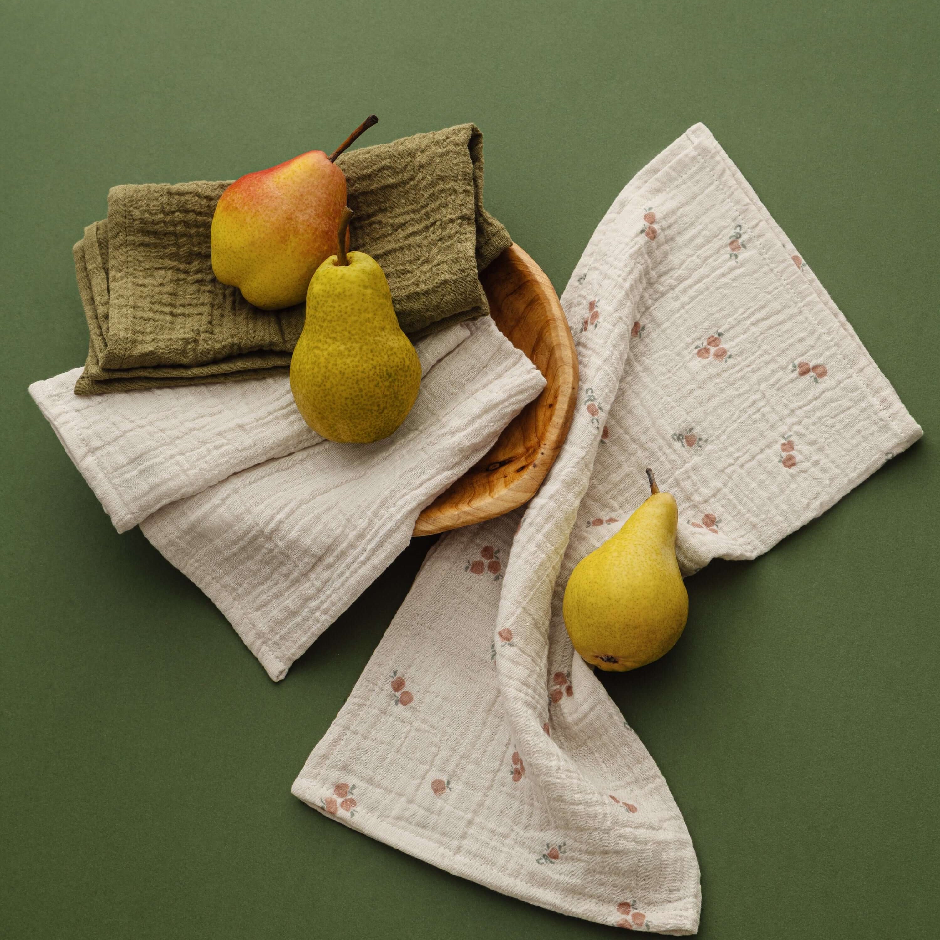 Pomme Burp Cloths displayed with organic muslin and decorative pears on a green background.