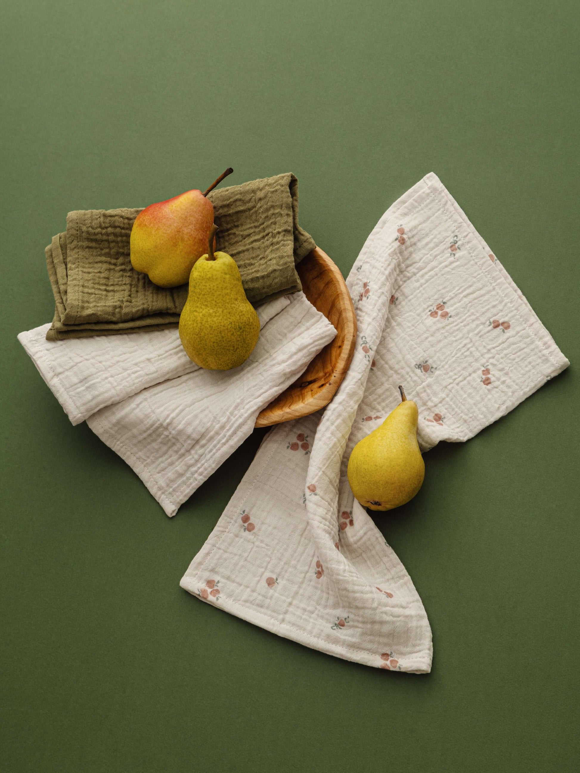 Pomme Burp Cloths displayed with organic muslin and decorative pears on a green background.