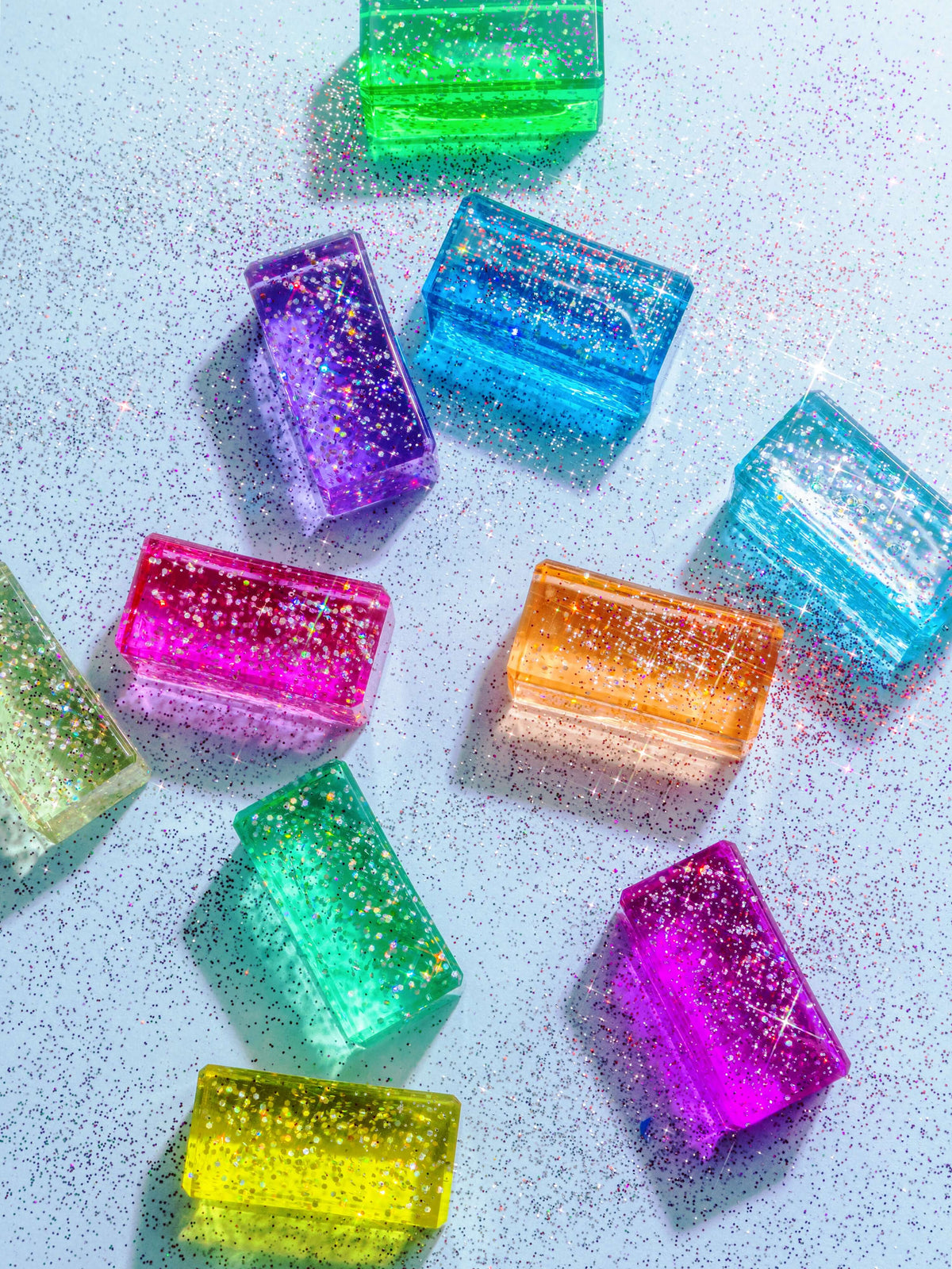 Veda glitter acrylic building blocks in various colors, featuring shimmering glitter, on a glittery background.